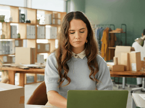 Hnědovlasá mladá paní sedí v knihovně a před sebou má počítač