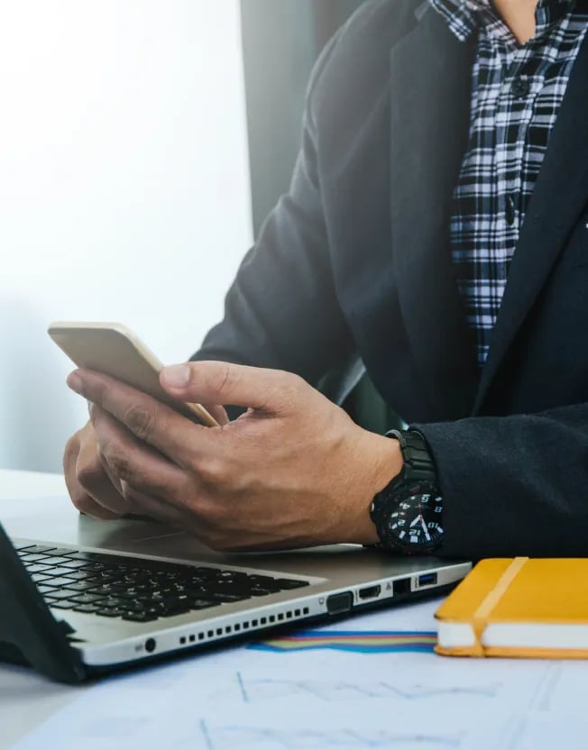 Byznysmen u notebooku s mobilem v ruce